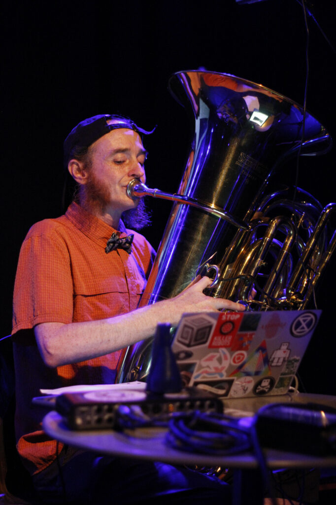 Charles Hutchins playing the tuba, looking at a laptop